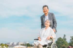 高齢女性が乗った車いすを高齢男性が押して笑顔で散歩する写真です。