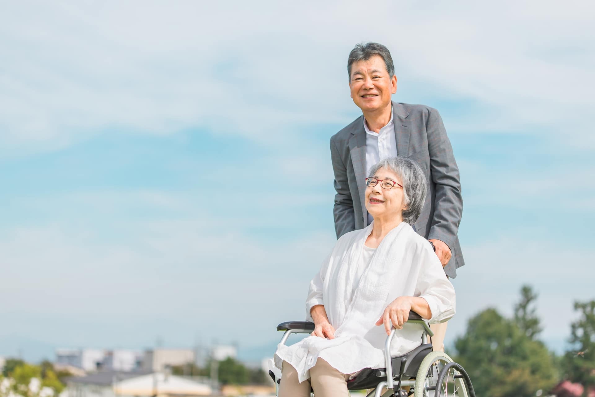 高齢女性が乗った車いすを高齢男性が押して笑顔で散歩する写真です。